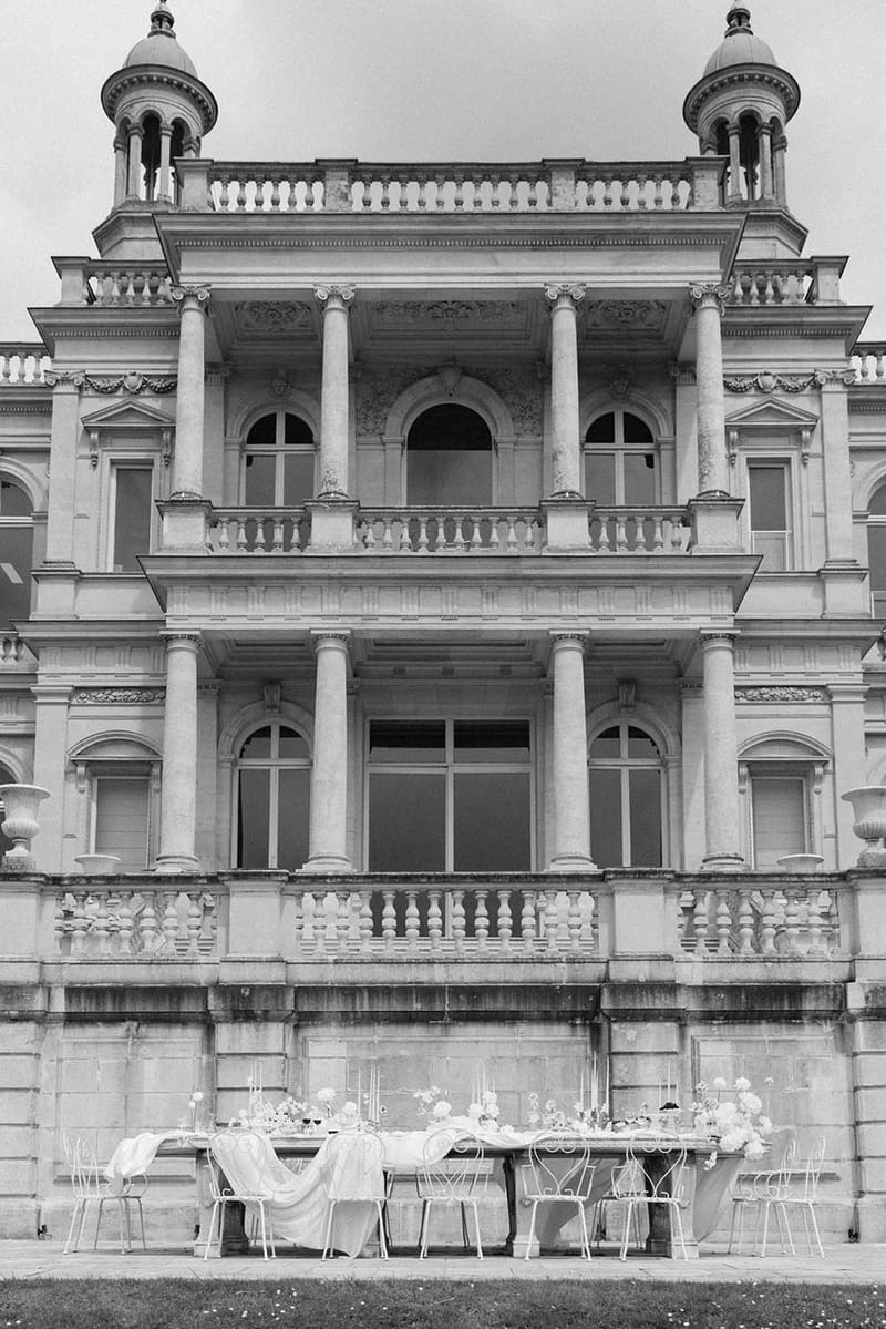 Black-and-white wide shot of reception table in front of grand classical chateau facade with columns and domed towers