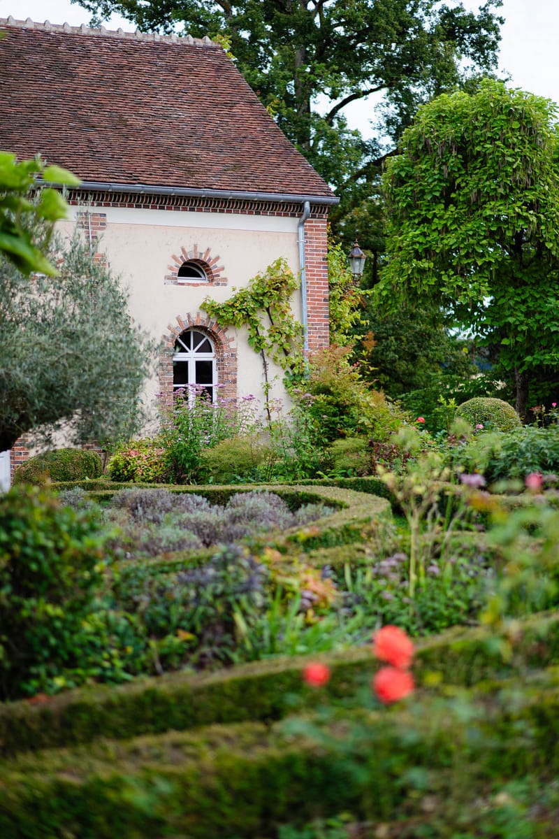 French country venue with cream walls, brick quoins, climbing vines, and formal knot garden with box hedging