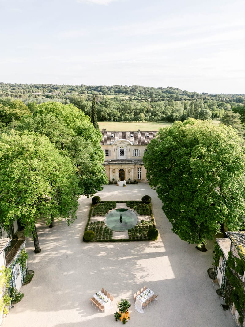 Aerial view of French chateau estate showing parterre garden, reflective pool, and reception tables on gravel forecourt