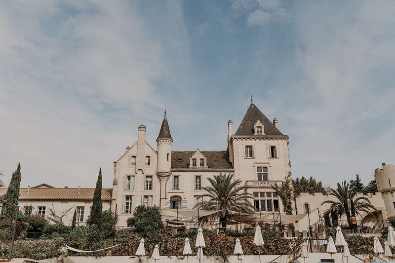 Cream stone chateau with twin turret towers, slate roofs, and terraced event area with umbrellas