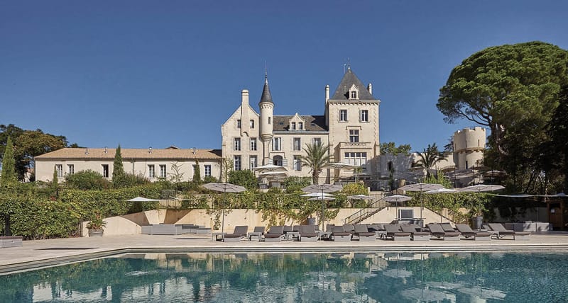 Chateau Les Carrasses exterior with limestone turrets, slate roofs, and poolside sun loungers