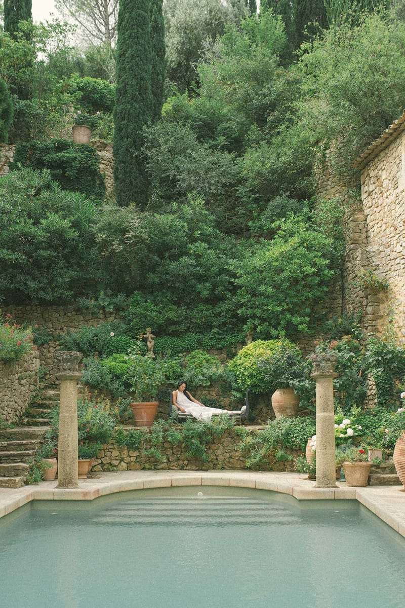 Bride on stone terrace behind rectangular pool at Provencal mas with limestone columns and tiered garden