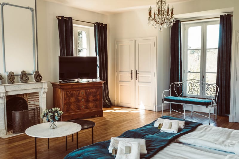 Guest bedroom in French chateau with white marble fireplace crystal chandelier and teal velvet accents