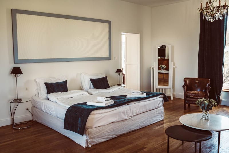 Venue bedroom suite with white linen bed, navy accents, crystal chandelier, and hardwood floors