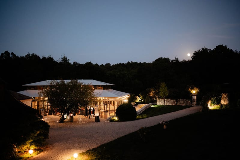 White marquee with festoon lights at dusk with full moon box hedging and gravel courtyard