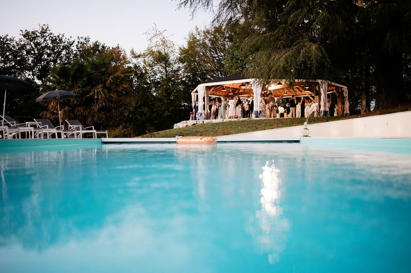 Dusk poolside cocktail with 35 guests under lit wooden pavilion with white draping and loungers