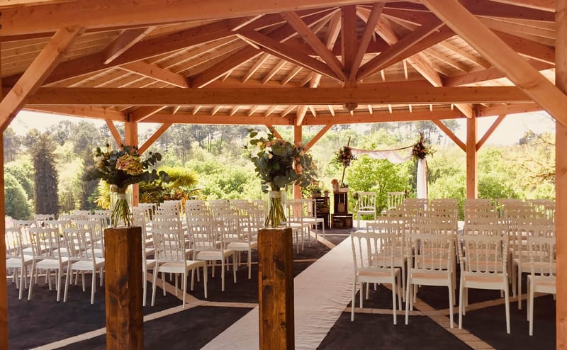 Wooden pavilion ceremony space with white chairs, floral aisle arrangements, and sheer fabric backdrop before guests arrive