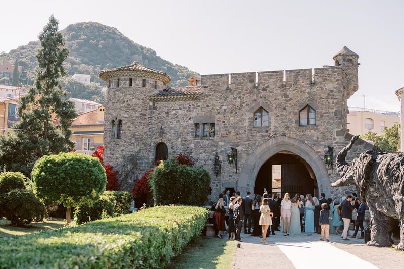 Guests gathering at the stone arched entrance of a medieval castle during cocktail hour with hillside town beyond