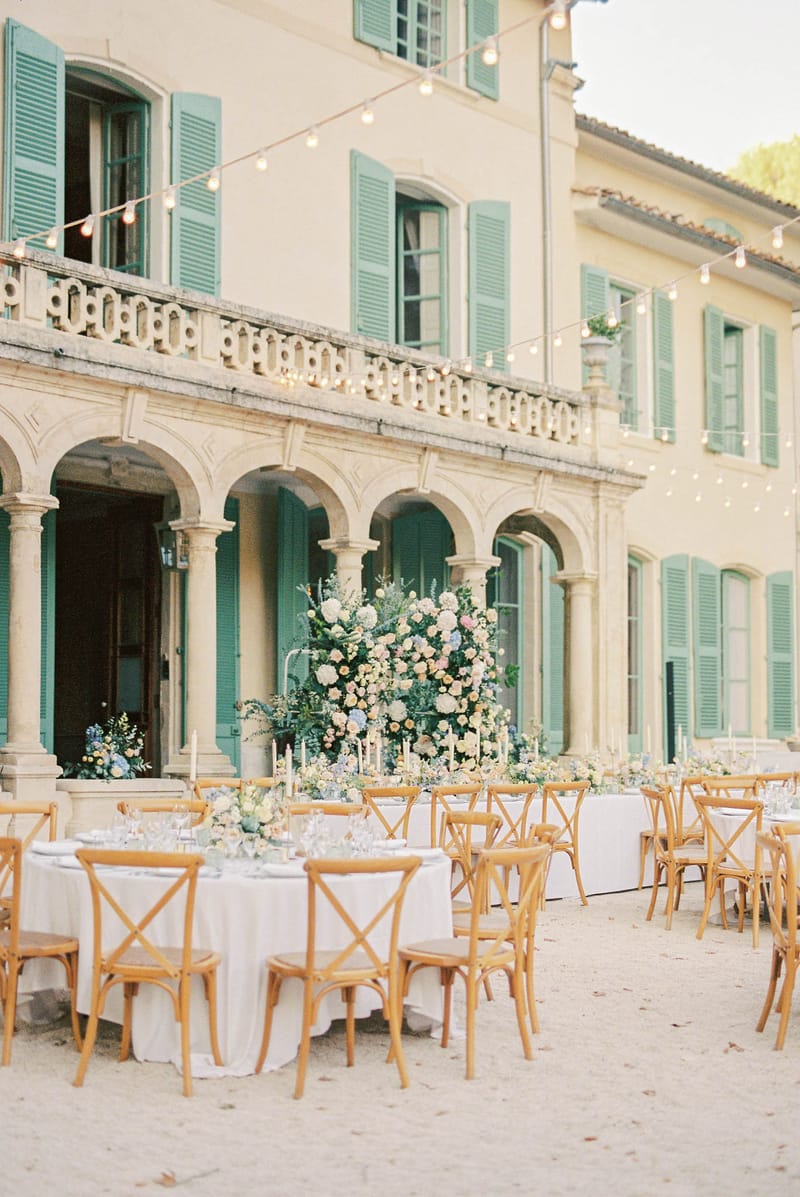 Outdoor courtyard reception with long and round tables, pastel florals, and string lights at French bastide