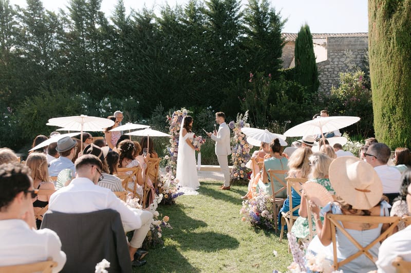 Forty guests at walled garden ceremony with colourful floral arch white parasols and wooden folding chairs