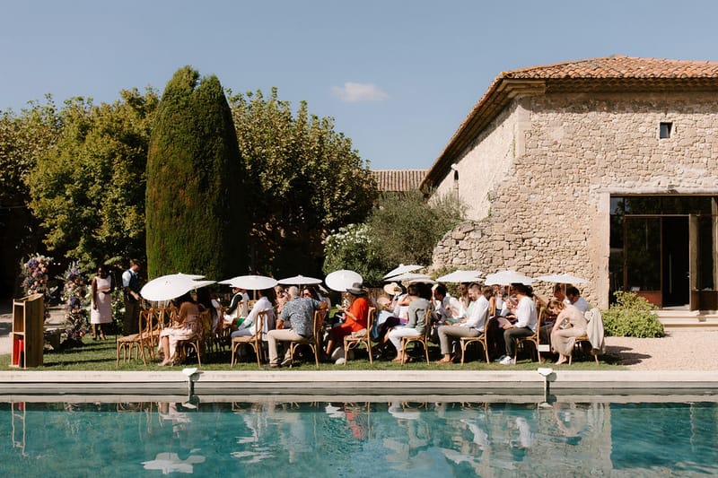 Poolside ceremony at Provencal stone mas with rattan chairs, parasols, and floral installation