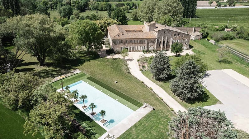 Aerial view of stone manor house with terracotta roof, swimming pool, manicured lawns, and surrounding vineyards