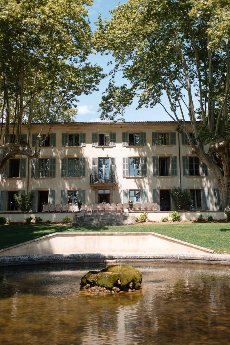 French bastide with sage green shutters viewed across a reflecting pool with ceremony chairs set on the terrace