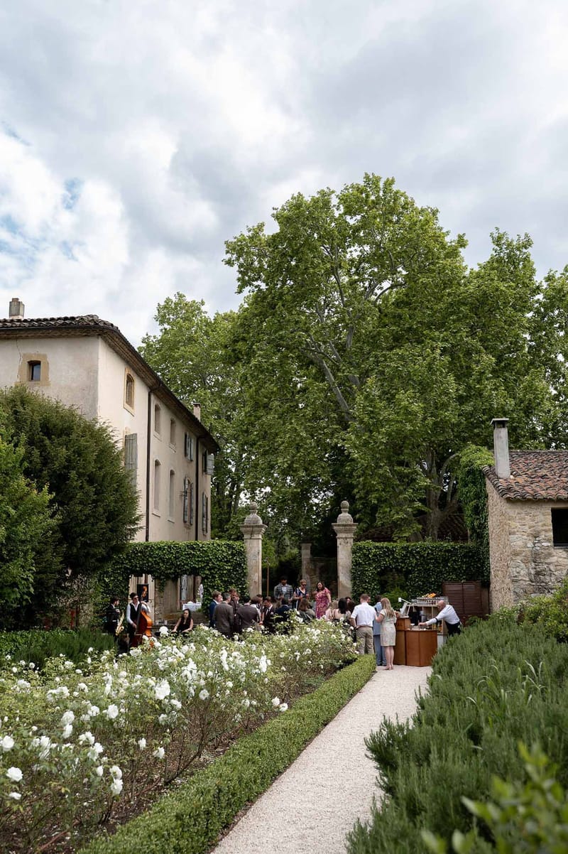 Guests mingling during cocktail hour in formal garden with live jazz band and bar station at French country estate