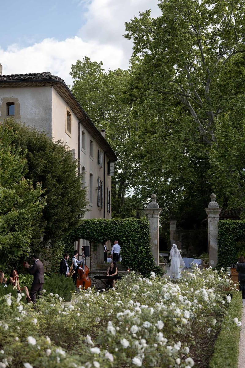 Jazz trio performs in formal rose garden as bride in veil enters through stone gate at French estate