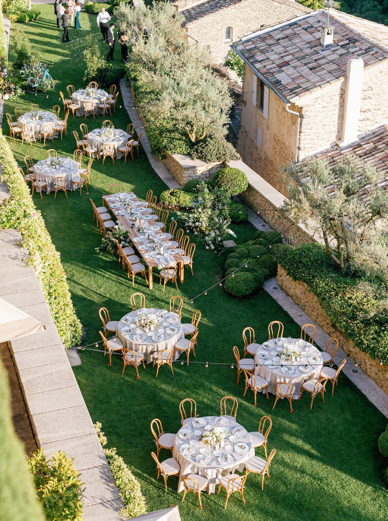 Aerial view of round and farm tables with ivory florals bistro chairs and string lights on lawn