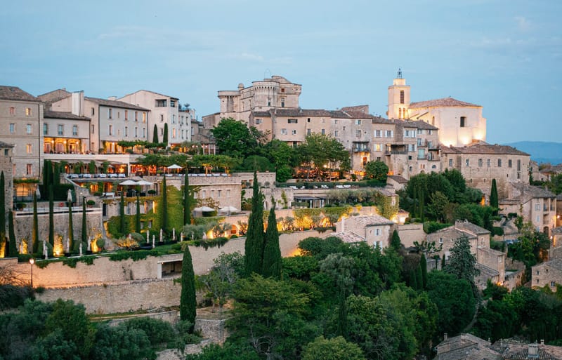 Hilltop Provencal village at dusk with lit terraces, Romanesque bell tower, and medieval chateau tower