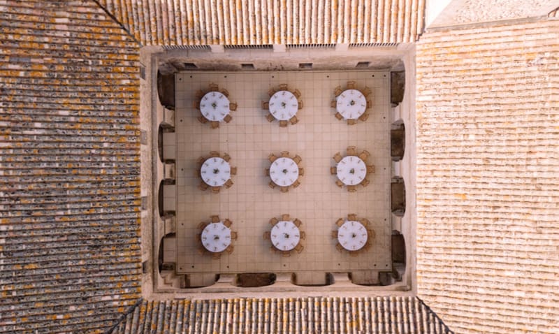 Aerial view of nine round tables in stone courtyard with terracotta roofs and arched recesses