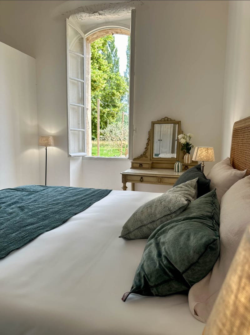 Guest bedroom with rattan headboard, green velvet cushions, gilt vanity, and arched stone window