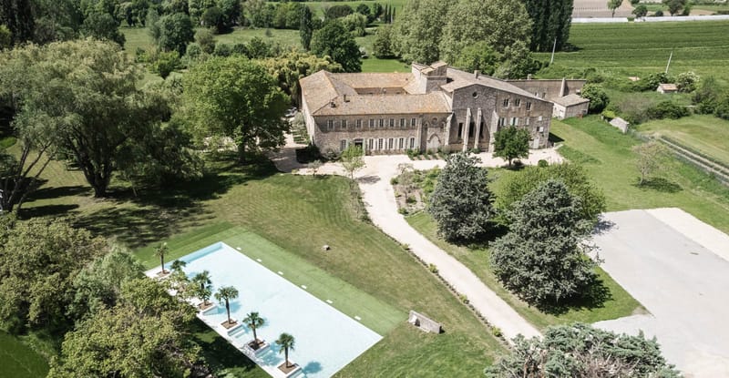 Aerial drone view of a stone Provencal property with terracotta roofs, infinity pool, and surrounding vineyards