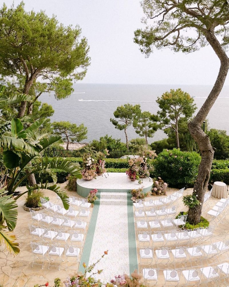 Elevated view of seaside ceremony with circular platform, green striped aisle, and curved seating