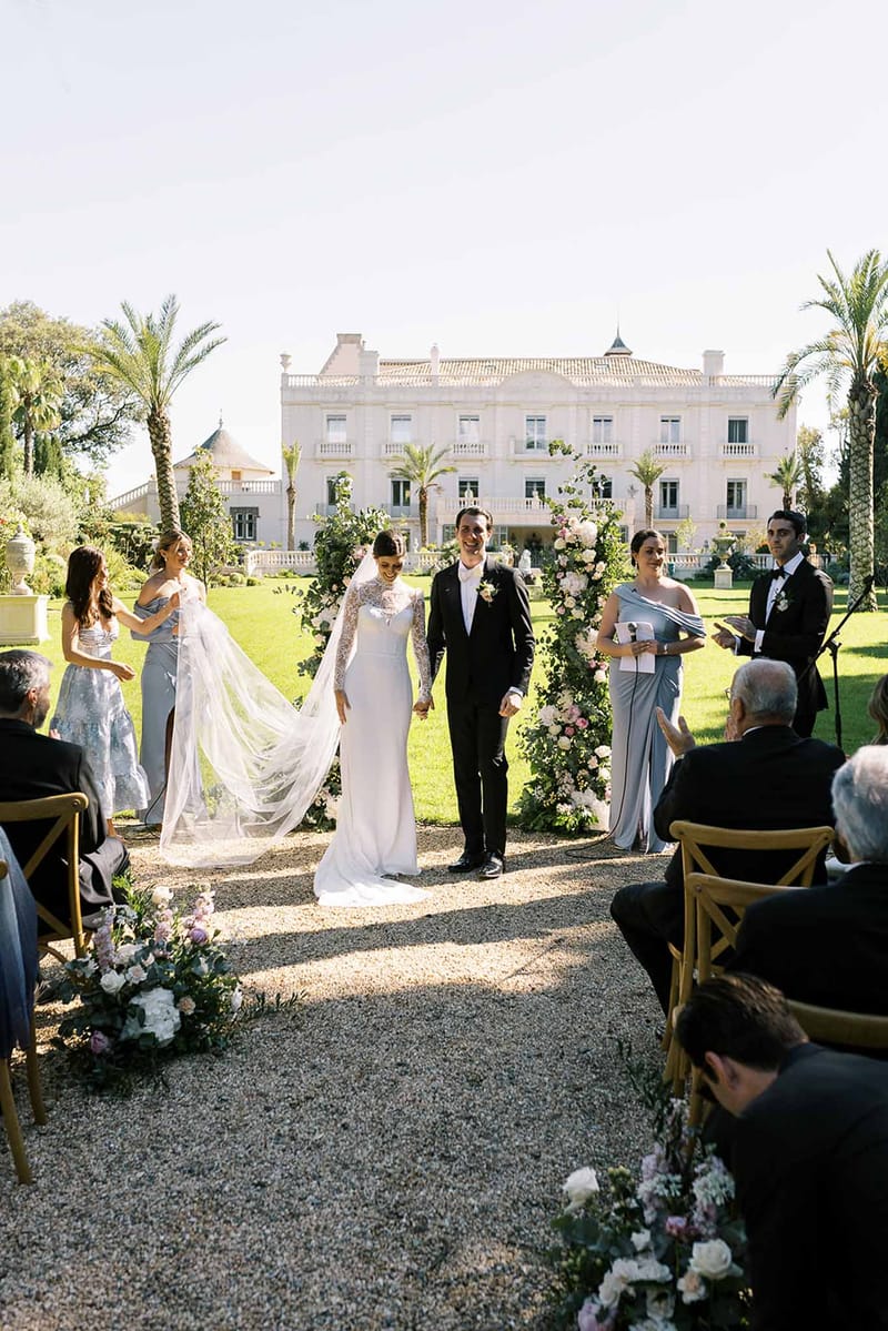Bride and groom walking up the aisle hand in hand after ceremony with bridesmaids in dusty blue at neoclassical chateau