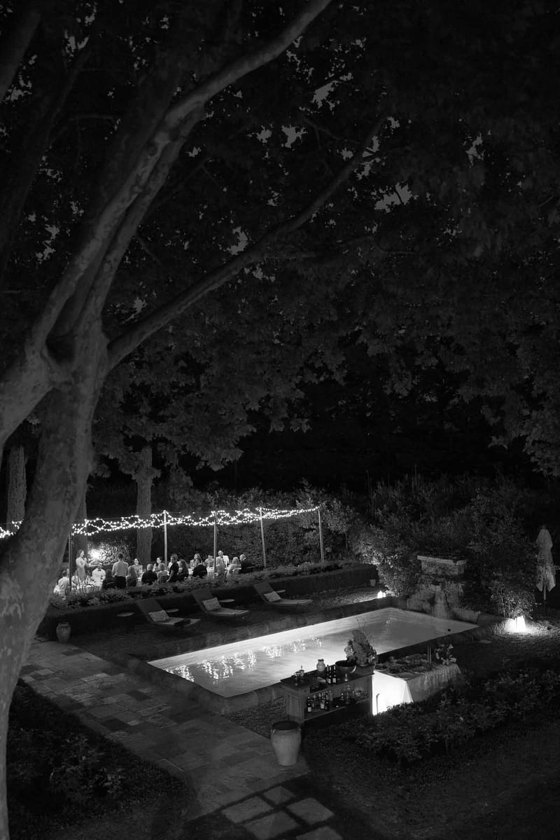 Black and white evening reception with fairy-lit pergola, poolside bar, and 30 guests in garden
