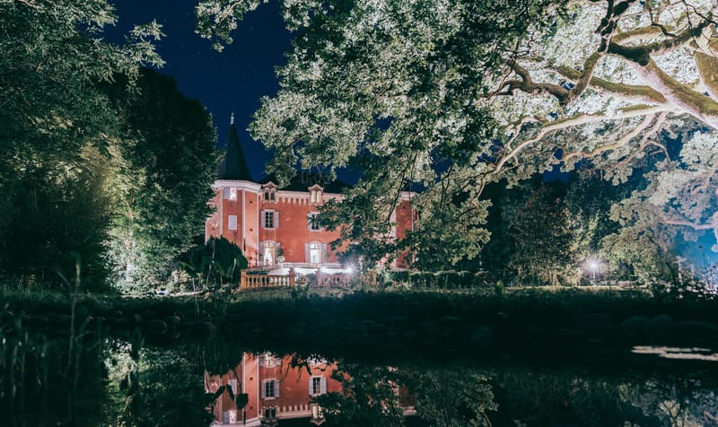 French chateau with terracotta brick facade reflected in ornamental pond at night with blue sky
