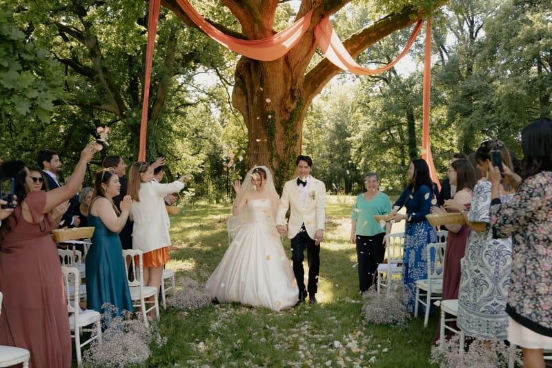 Bride and groom walking back up the aisle as guests toss flower petals during outdoor garden ceremony recessional