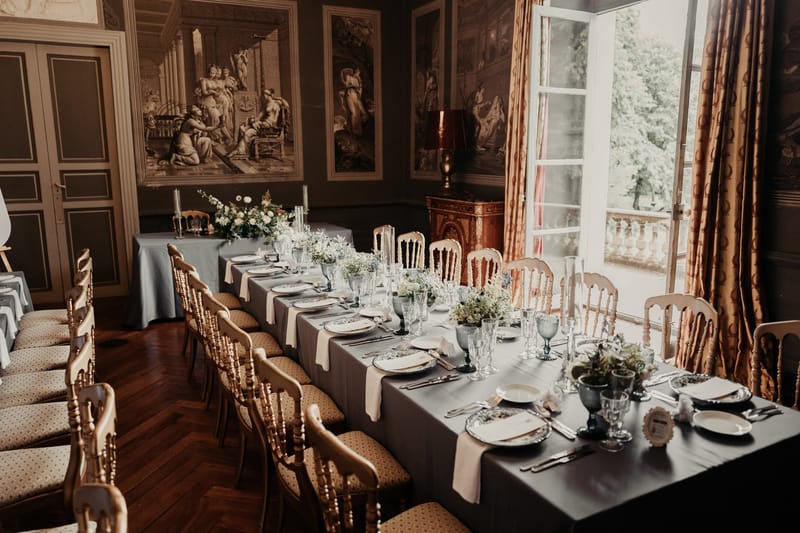 Long banquet table in French chateau with slate blue linens, white floral centerpieces, and grisaille murals