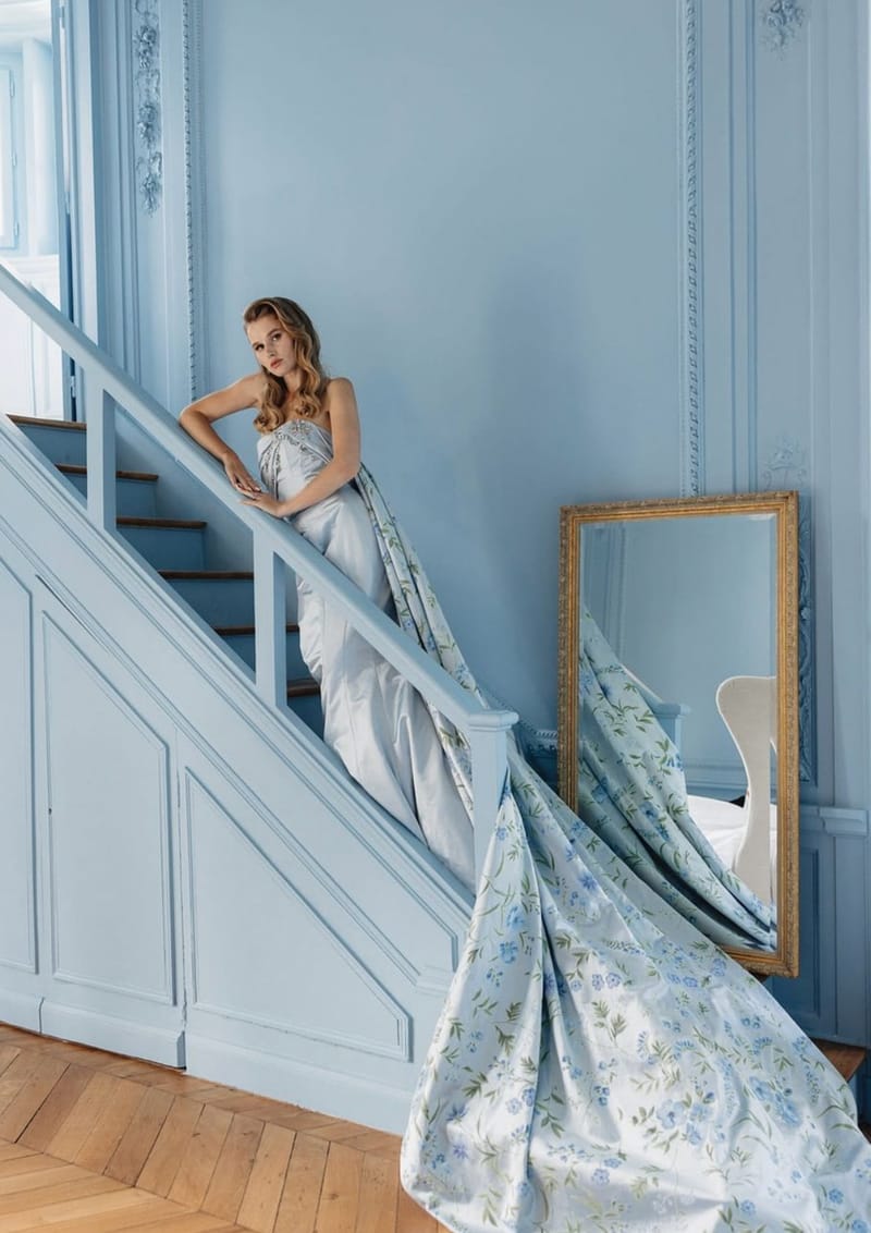 Bride in silver-blue gown with botanical print train cascading down powder blue paneled chateau staircase