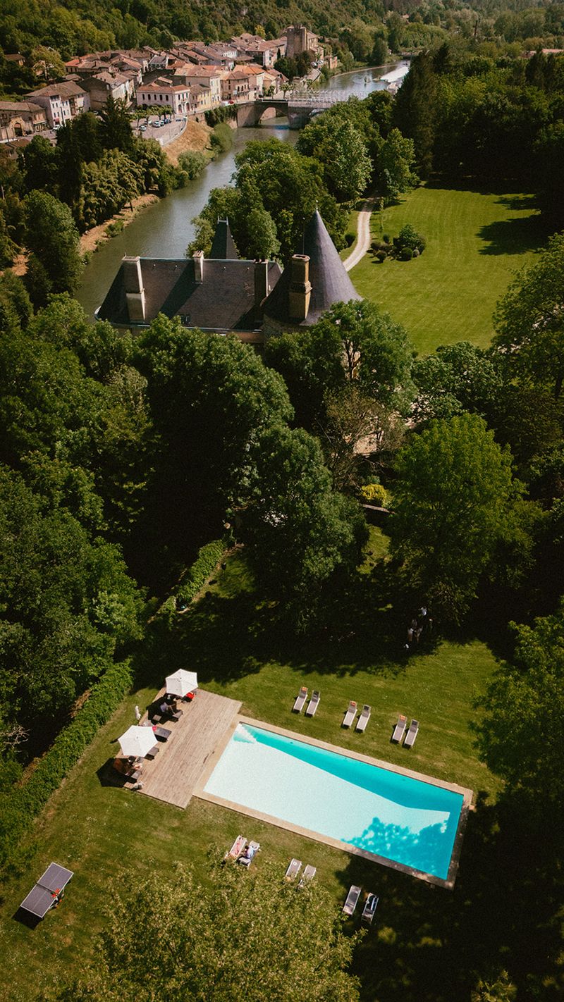 Aerial drone view of French chateau estate with pool terrace, river, and village in background