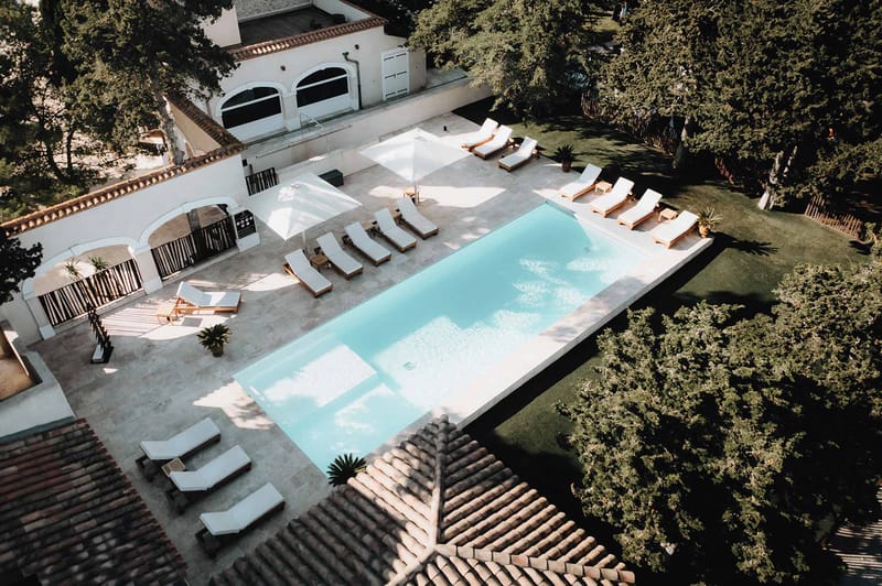 Aerial view of white Provencal villa with infinity pool, teak loungers, and arched terrace doorways