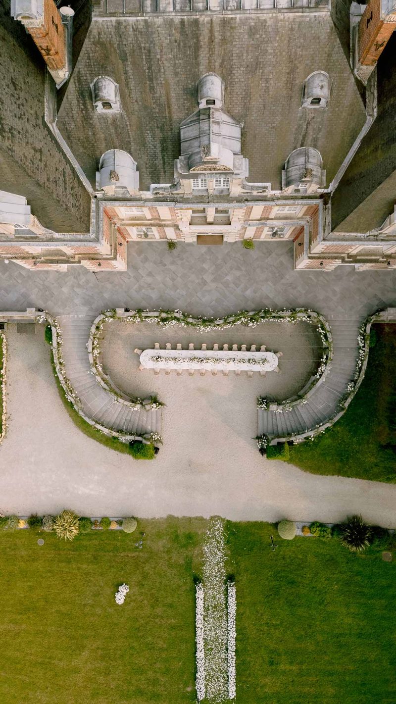 Aerial view of chateau courtyard with long reception table, curved floral balustrade, and petal-lined aisle