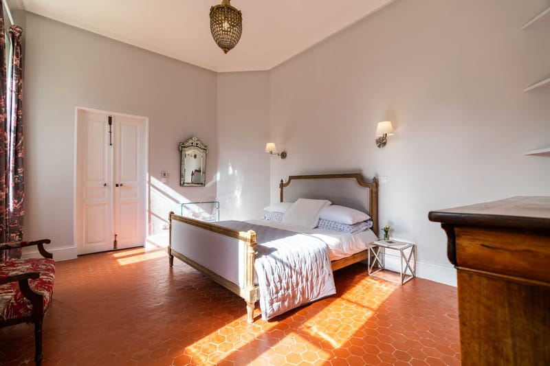Chateau bedroom with terracotta tiles carved Louis XVI bed gold chandelier and red toile chair