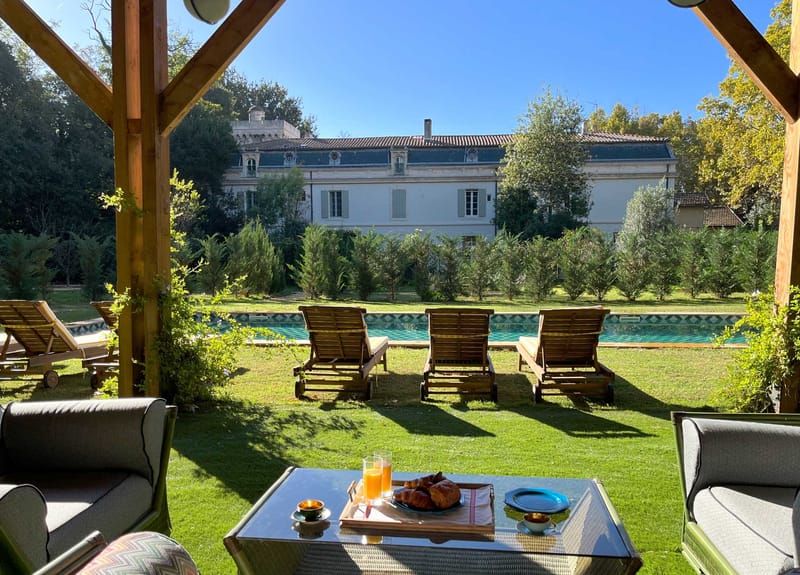 Breakfast pergola with pool loungers and chateau facade framed through wooden beams