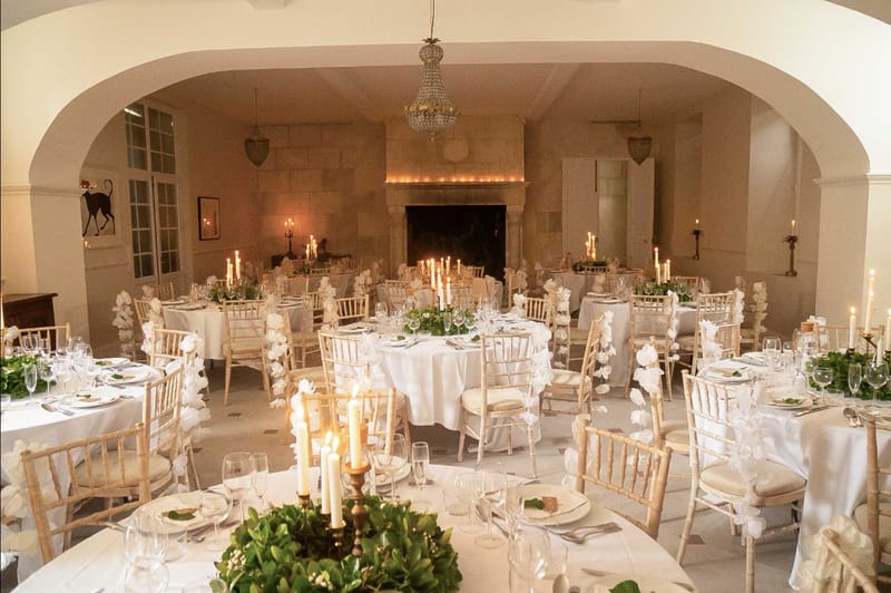 Chateau dining room with round tables, white orchid chair decor, brass candelabras, stone fireplace and chandelier