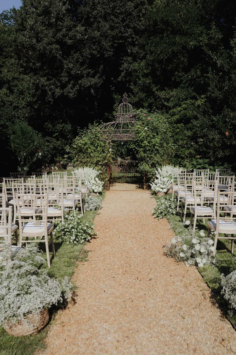 Garden ceremony with chiavari chairs, baby's breath aisle borders, and wrought-iron gazebo with climbing roses