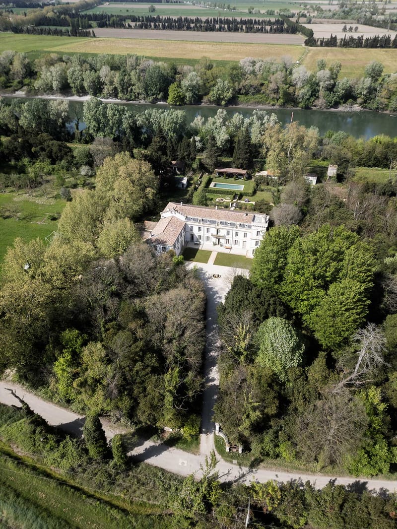 Aerial view of French chateau with terracotta roof, swimming pool, formal gardens, and river alongside