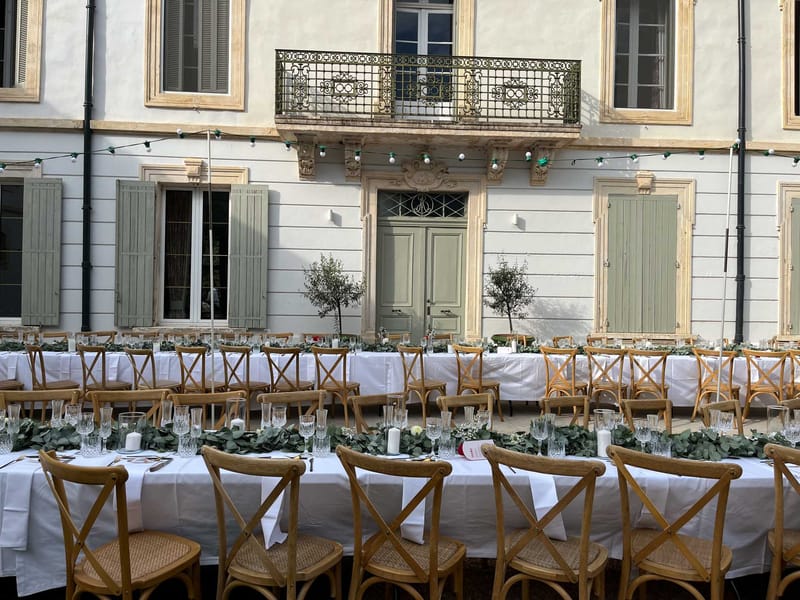 Bastide courtyard with long banquet tables, eucalyptus garland, olive tree centerpieces, and globe lights