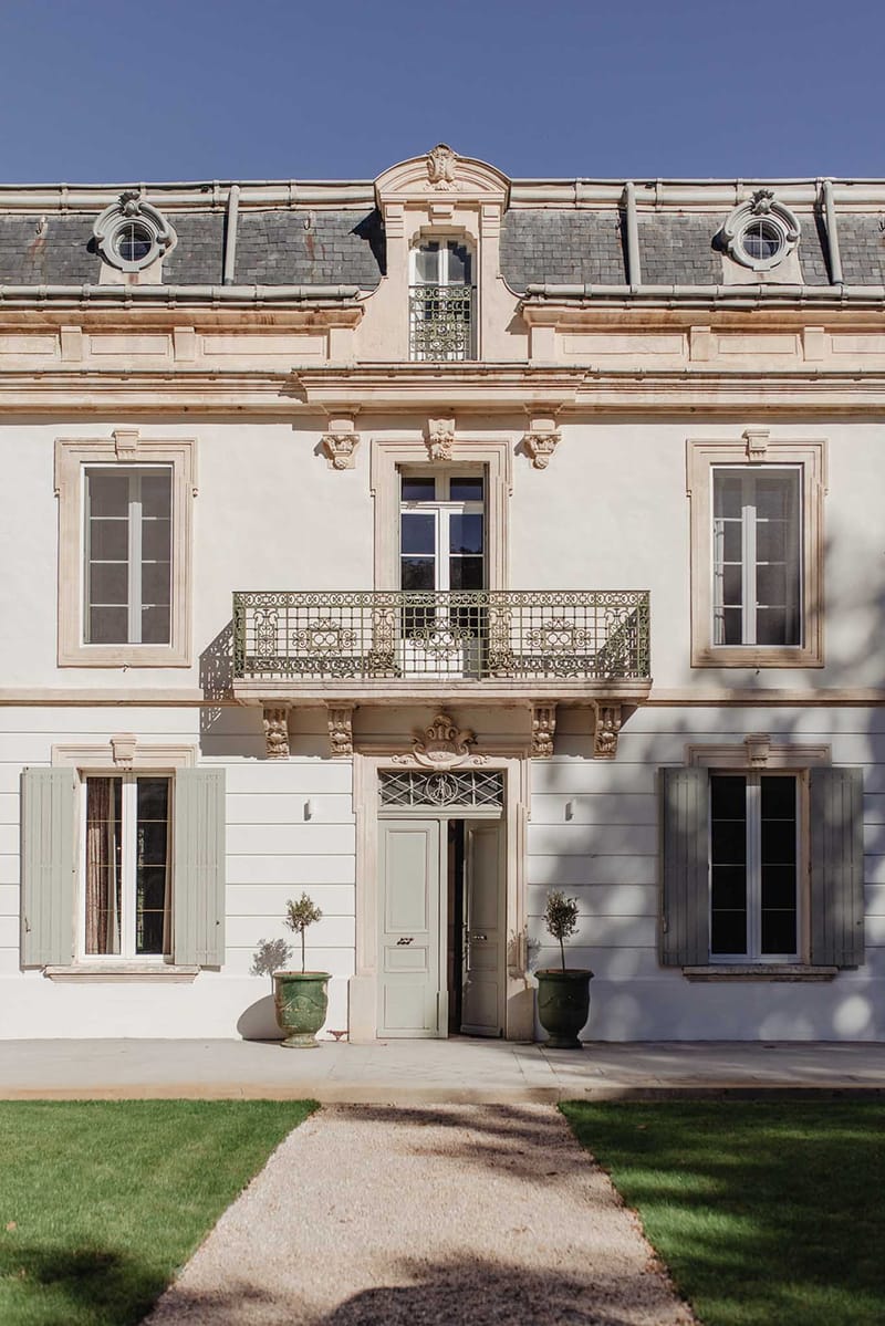 Three-storey cream chateau with sage shutters iron fanlight carved cartouche and topiary urns