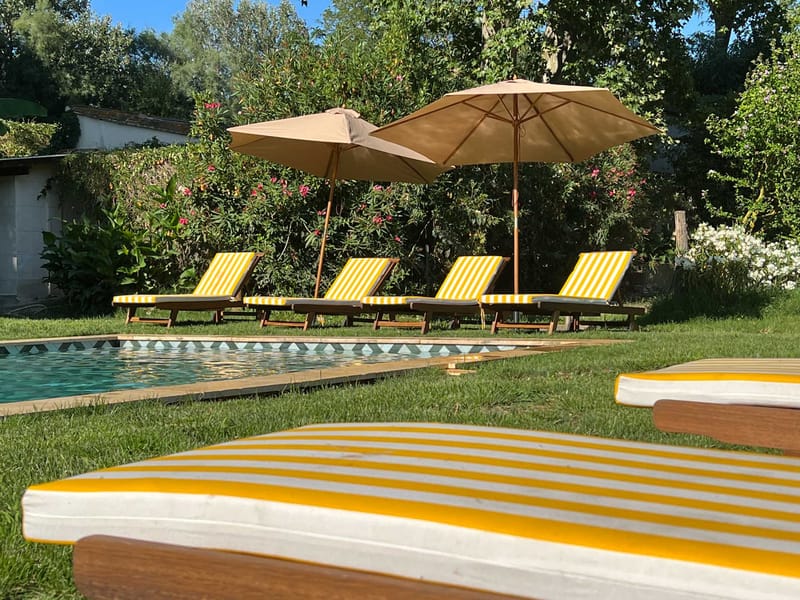 Pool terrace with yellow and white striped loungers tan canvas umbrellas and rectangular swimming pool on estate grounds