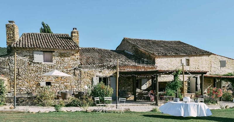 Rustic French stone farmhouse with festoon lights, pergola, white cocktail tables, and Provencal courtyard setting