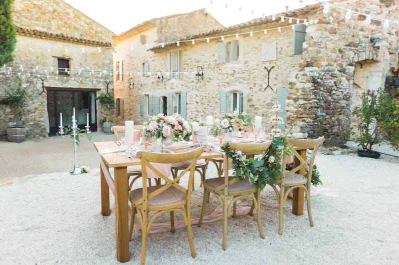 Styled outdoor reception table with blush pink runner, pink glassware, rose centerpieces, and fairy lights in a Provencal ...