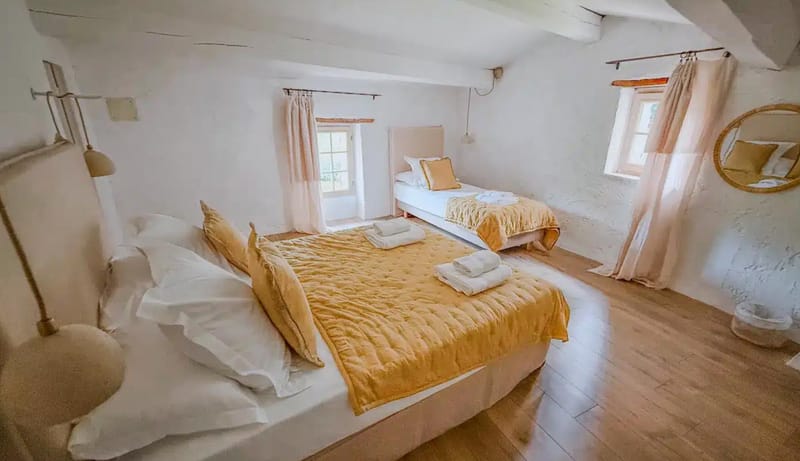 Guest bedroom with mustard yellow bedspreads, exposed wooden beams, and blush curtains in Provencal venue