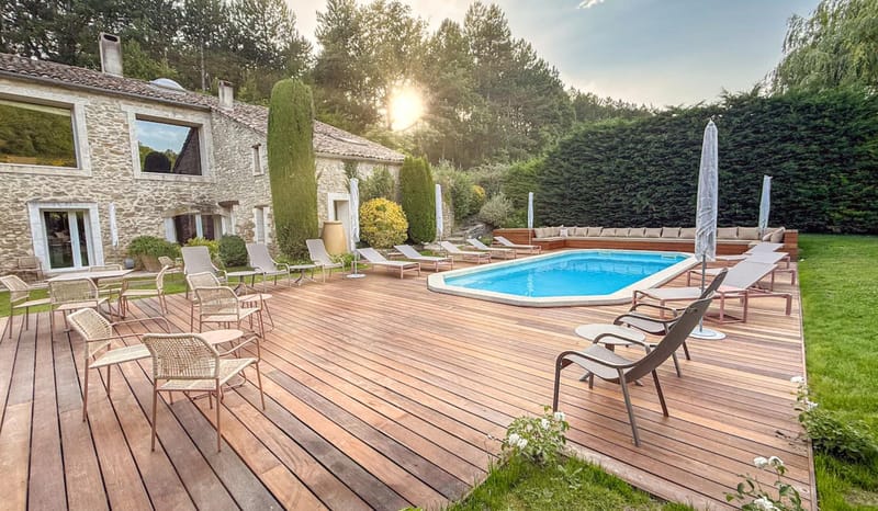 Stone mas venue with wooden deck, oval swimming pool, sun loungers and parasols at golden hour in Provence