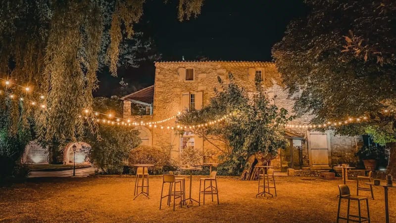 Nighttime Provencal mas courtyard with bistro string lights high cocktail tables and golden limestone walls