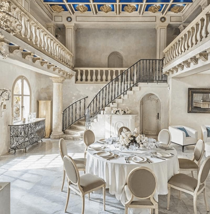 Double-height chateau hall with painted blue and gold ceiling limestone gallery and round reception table