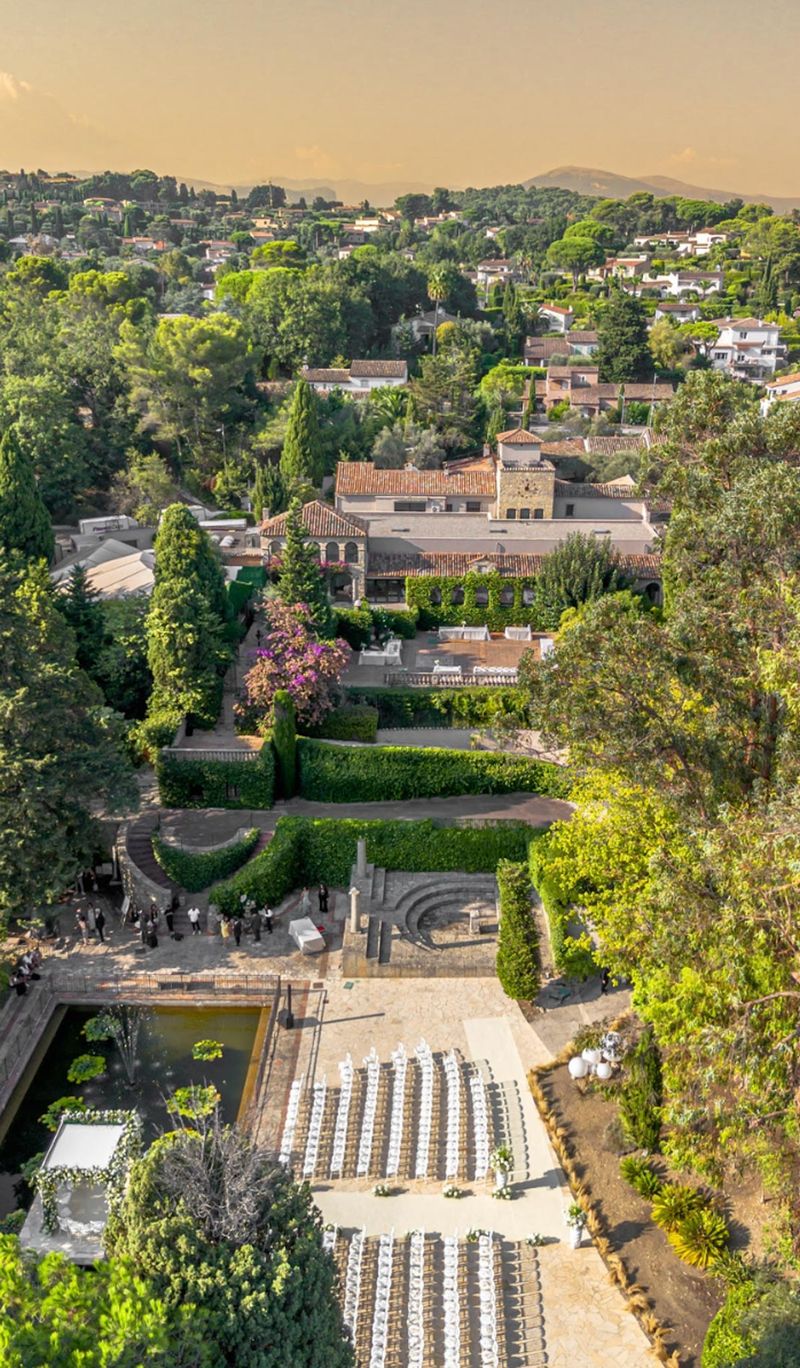 Aerial golden hour view of Provencal estate with ceremony seating, parterre gardens, and clock tower