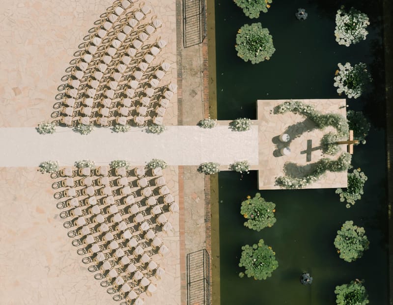 Aerial ceremony on terracotta terrace with 100 gold chairs, white aisle runner, and circular floral arch